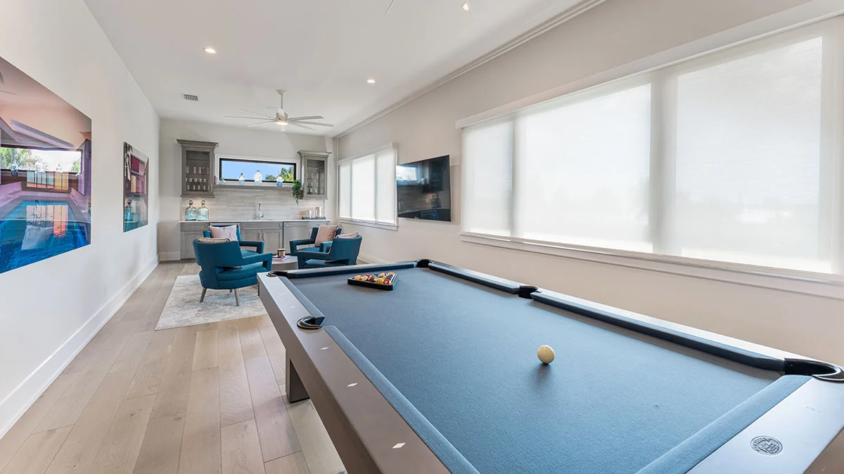Light-filtering roller shades along the windows of a game room with a pool table and blue chairs