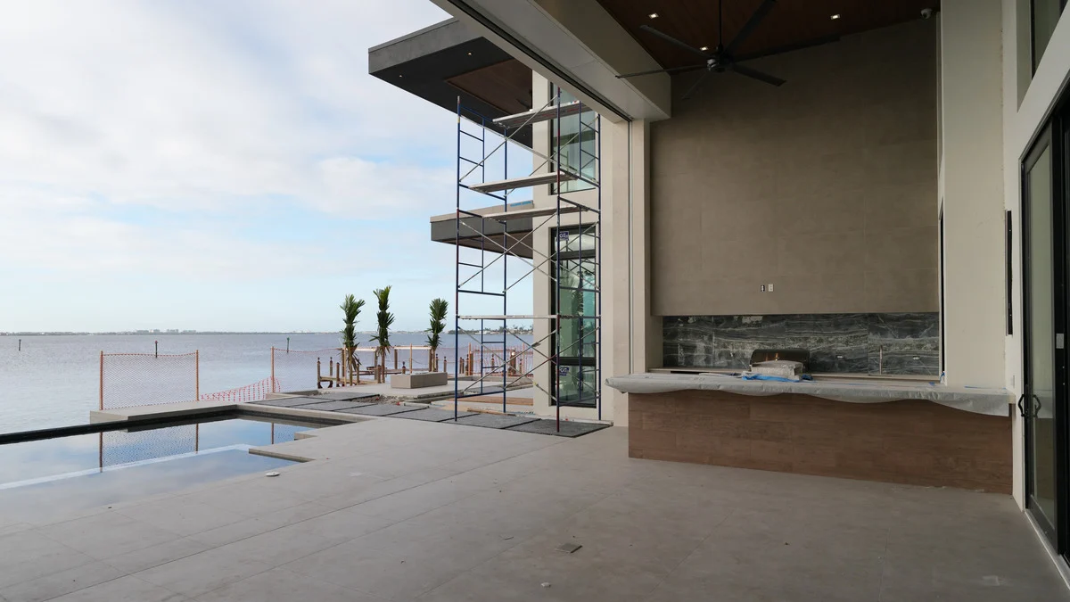 Unfinished covered outdoor kitchen beside a waterfront pool with scaffolding near the roof
