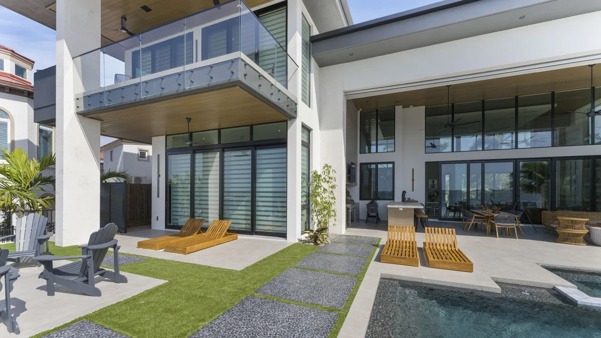 Completed pool patio with lounge chairs, rear window walls and bedroom shades visible through the glazing