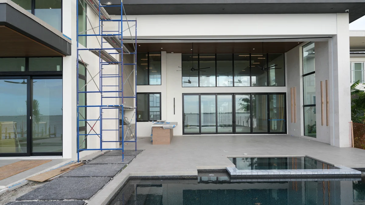 Pool and spa beside an unfinished covered patio and two-story rear window wall