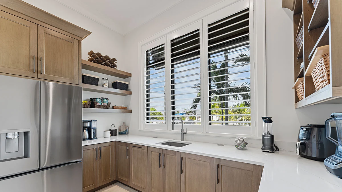 Plantation shutters controlling light and privacy in a coastal kitchen