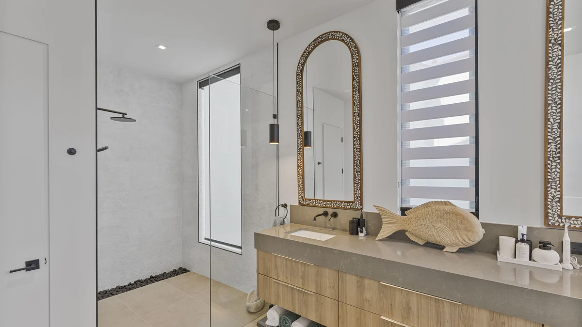 Bathroom shower and vanity with a covered shower window and a striped shade beside the mirror