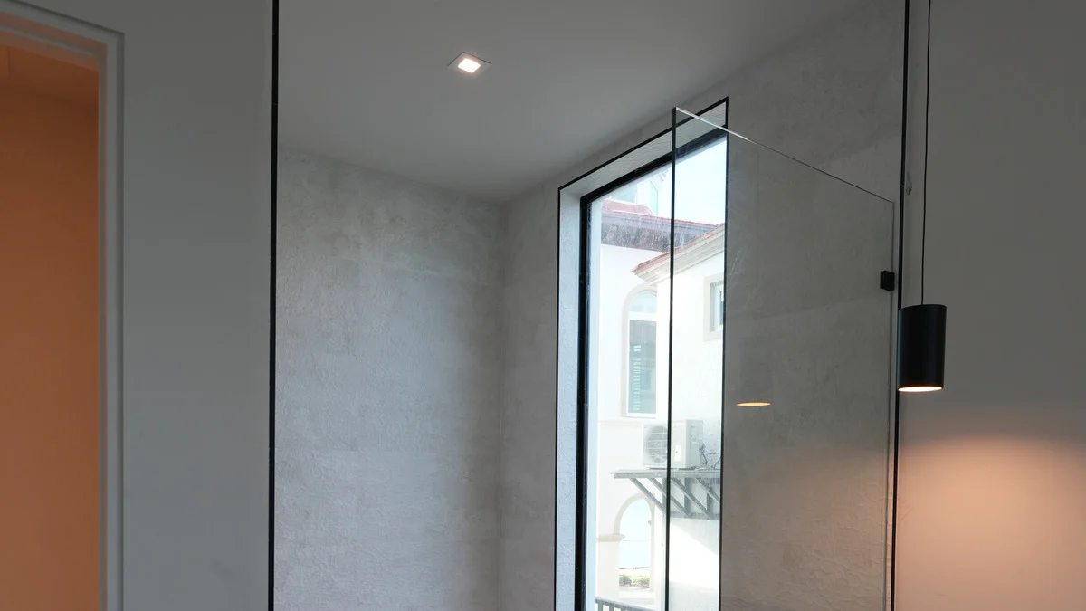 Tall uncovered shower window behind a glass shower screen beside a bathroom pendant light