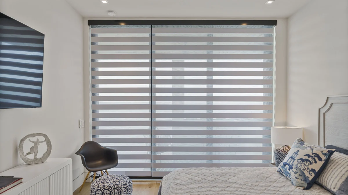 Zebra shades lowered over balcony doors beside a bed with blue accent pillows