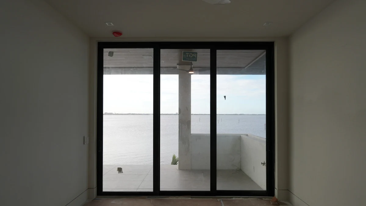 Uncovered three-panel balcony doors in an unfinished bedroom overlooking the water