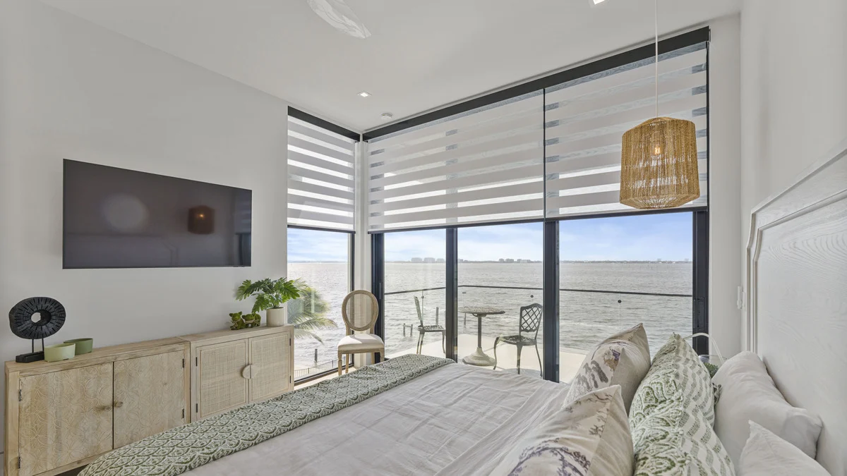 Partially raised zebra shades over corner balcony doors beside a bed with green accent pillows