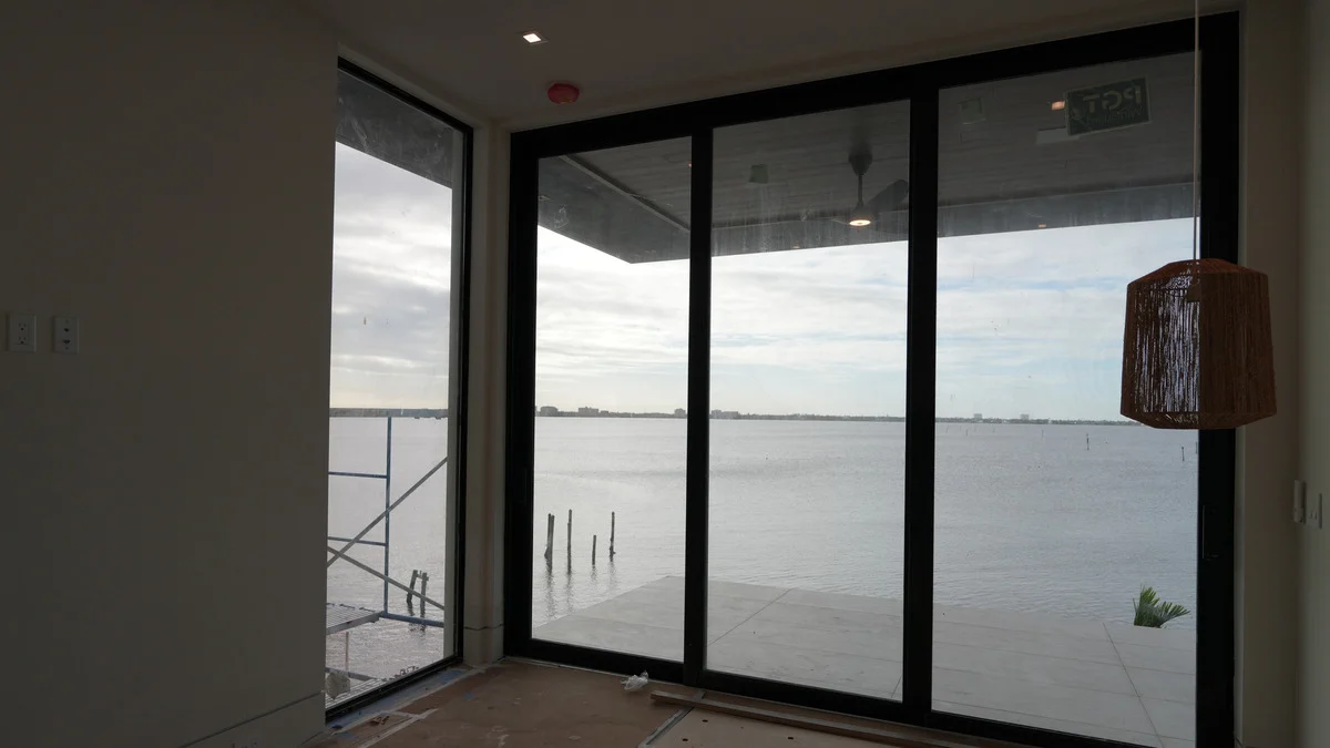 Uncovered corner balcony doors beside a woven pendant light in a bedroom under construction