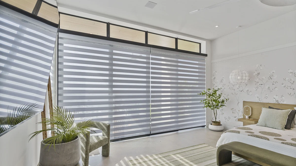 Zebra shades on corner glass doors beside the bed and a potted plant