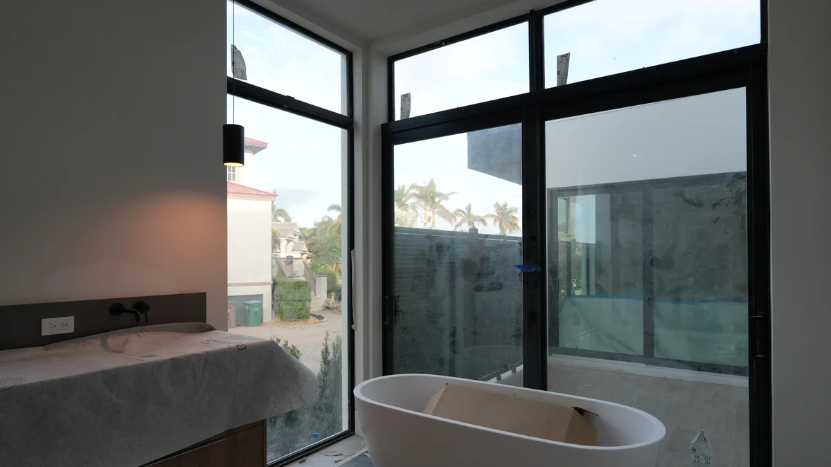 Uncovered corner windows behind a freestanding bathtub beside an unfinished vanity